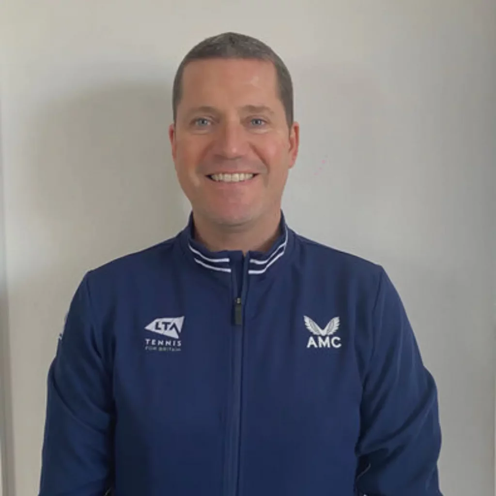 Chris smiling at the camera, with brown hair and blue tracksuit top on