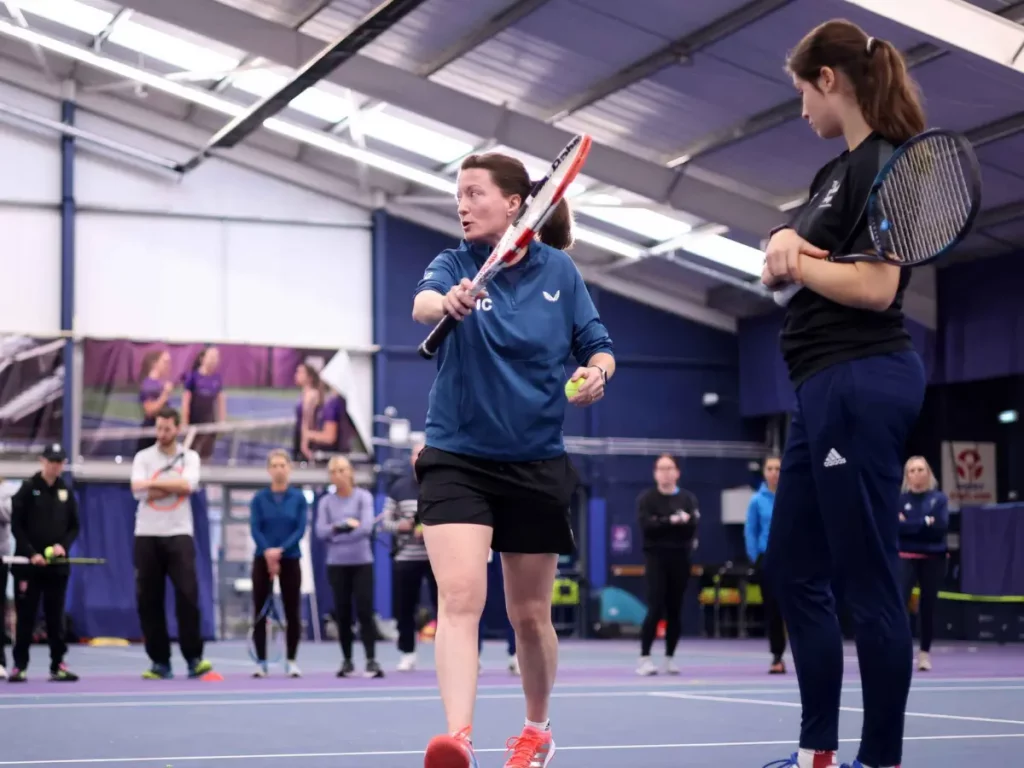 Tutor showing backhand volley movement, in front of coaches on course.