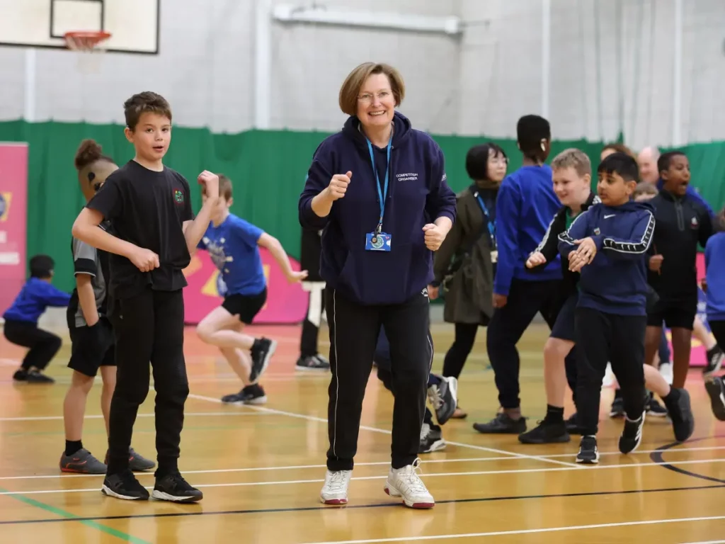 School teacher being active and getting students active, in a sports hall with basket ball ring in background