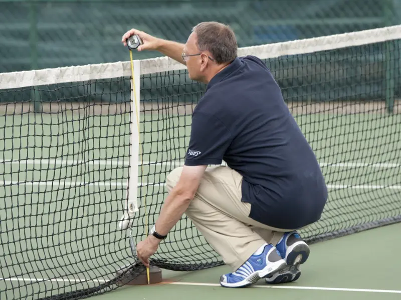 Tennis official measuring the height of the tennis net in the middle, with a tape measure