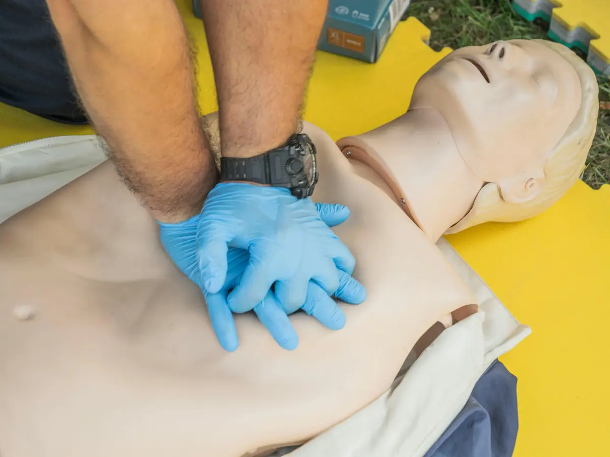 First aid trainer with hands in blue gloves showing CPR on a dummy