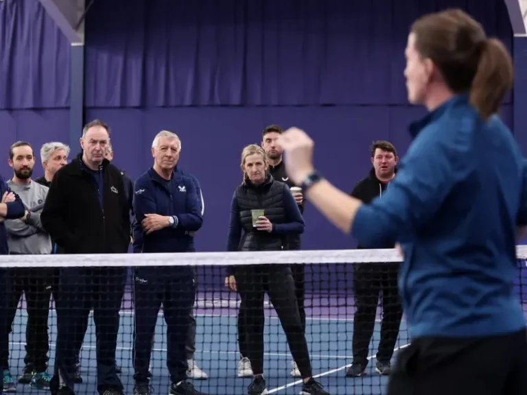 Tutor sharing info to a group of coaches, in front of tennis net