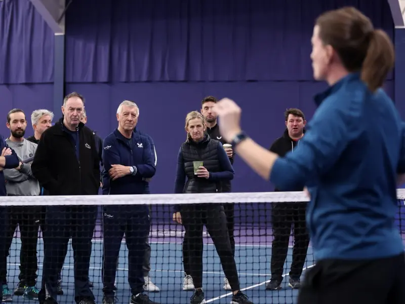 Tutor sharing info to a group of coaches, in front of tennis net