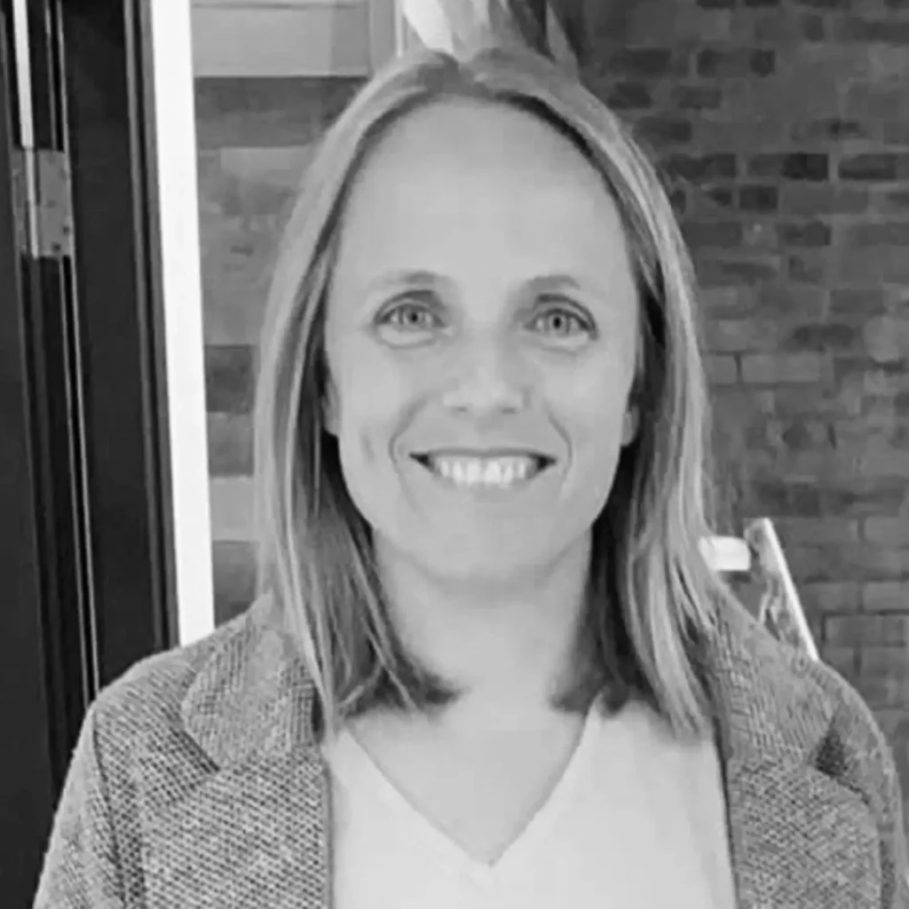 Lucy smiling at the camera, with blonde brown hair. Wearing jacket and white t shirt