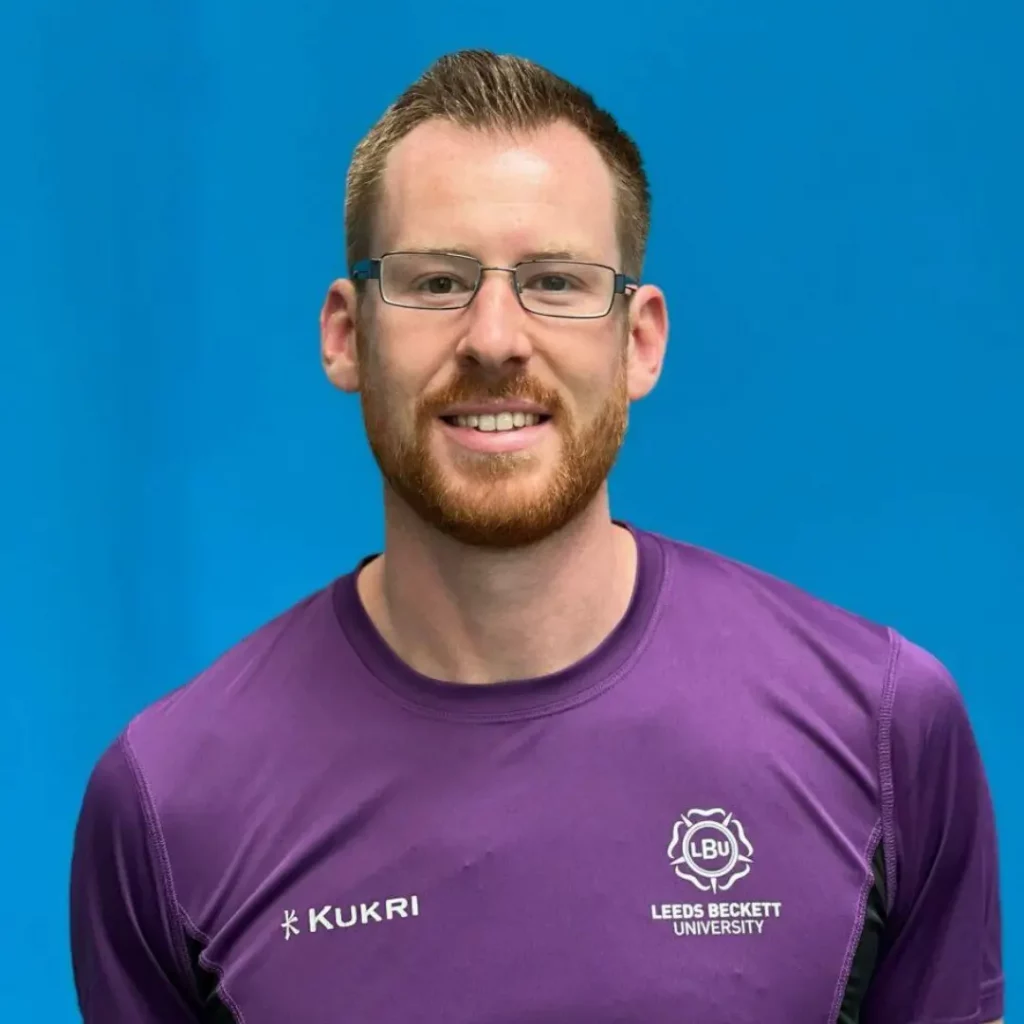 Paul smiling at camera with glasses on and wearing purple t shirt