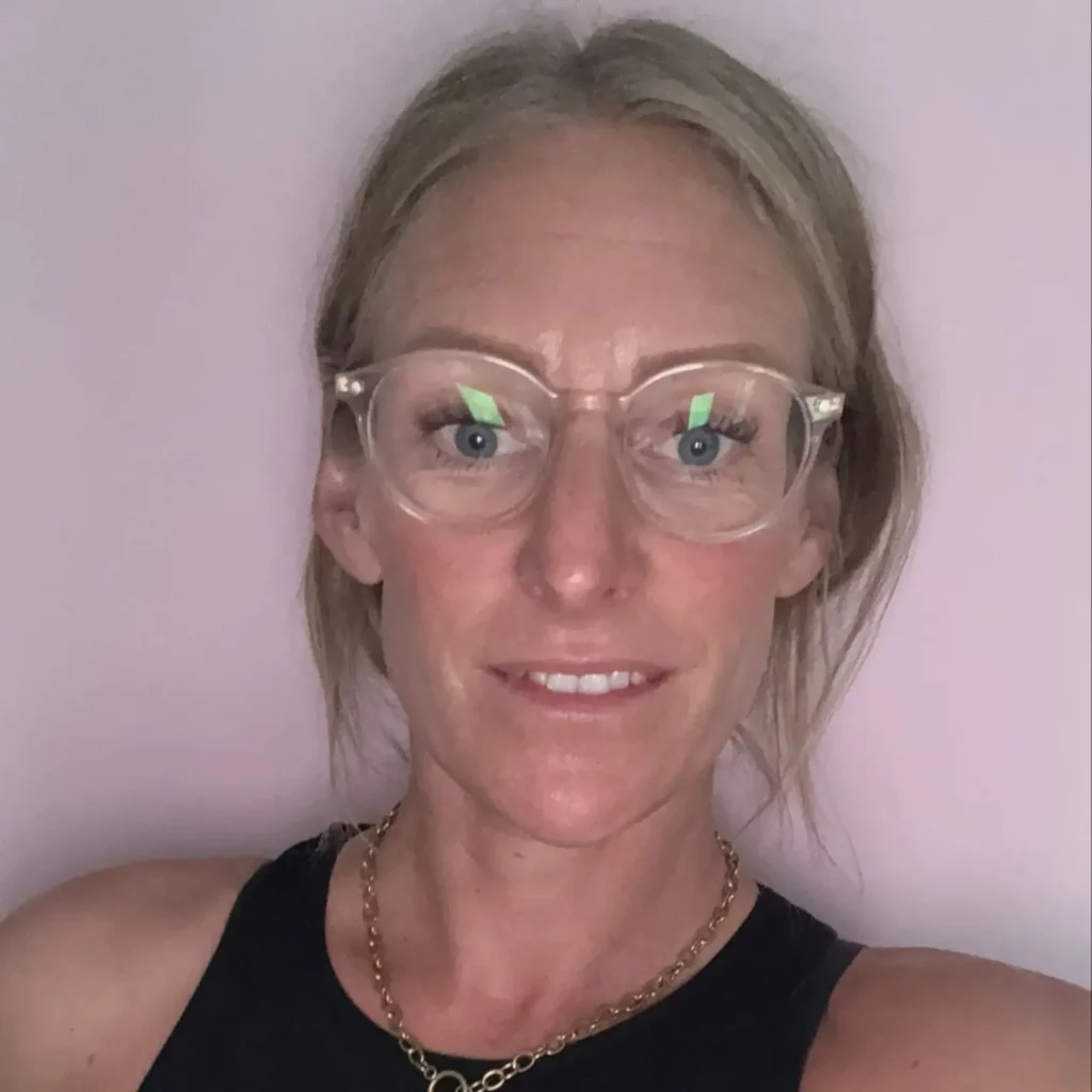 Sarah smiling at camera with hair tied back and wearing glasses.