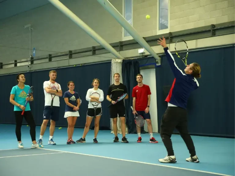 Coach showing serving demonstration with ball toss in air and racket behind head