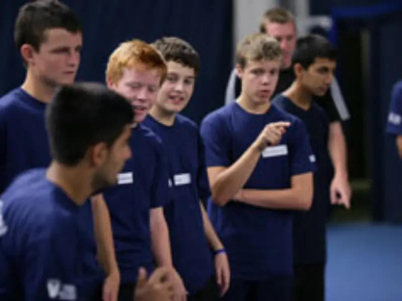 Young people with navy blue competition organiser t shirts on watching tennis at the side of court