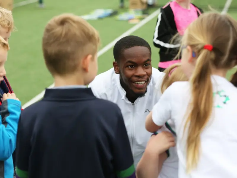 Coach crouched down to young player height, smiling and listening to group of children in front.