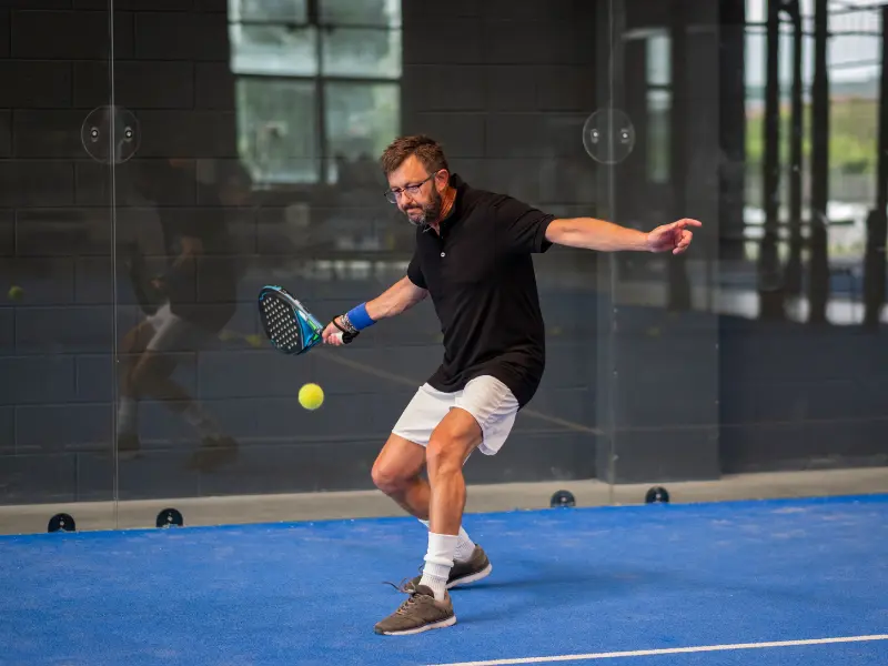 Male player hitting the padel ball off the back glass, towards the other side of court
