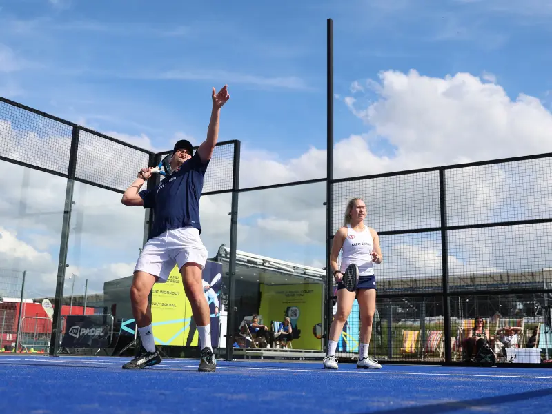 Male player on padel court, hitting overhead, with female player at net, nearby