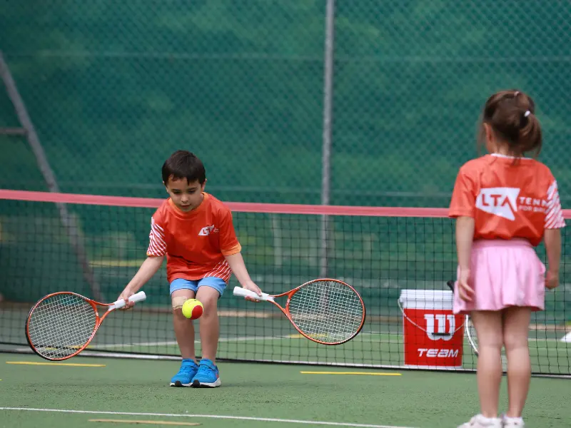 Red (8&U) players practicing catching ball with two rackets